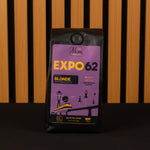 Purple coffee package labeled 'Expo 62 Blonde' against a wooden slatted background