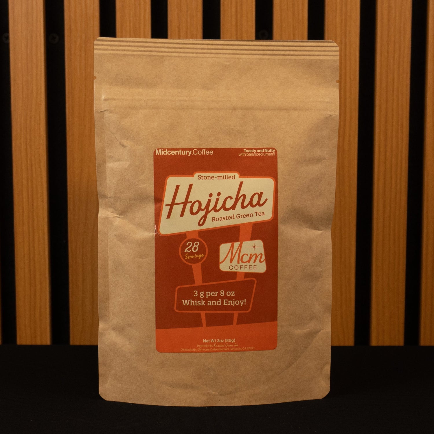 Kraft paper coffee bag with a red label featuring 'Hojicha' branding against a wooden slat background.