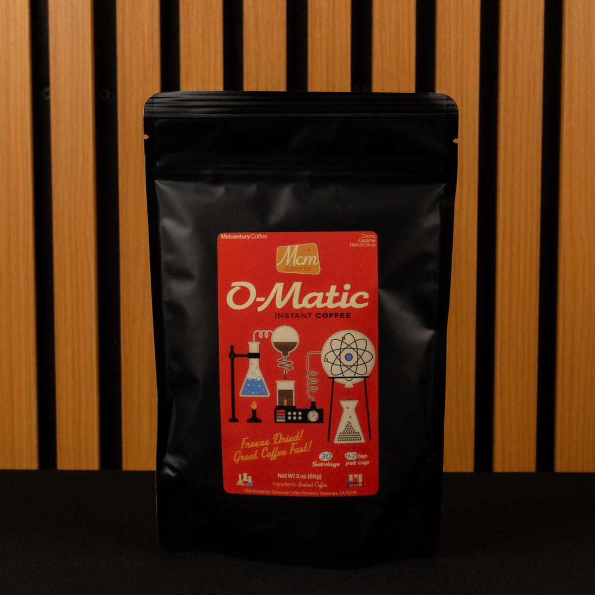 Black specialty grade Instant coffee bag with a red label featuring 'O-Matic' branding against a wooden slat background
