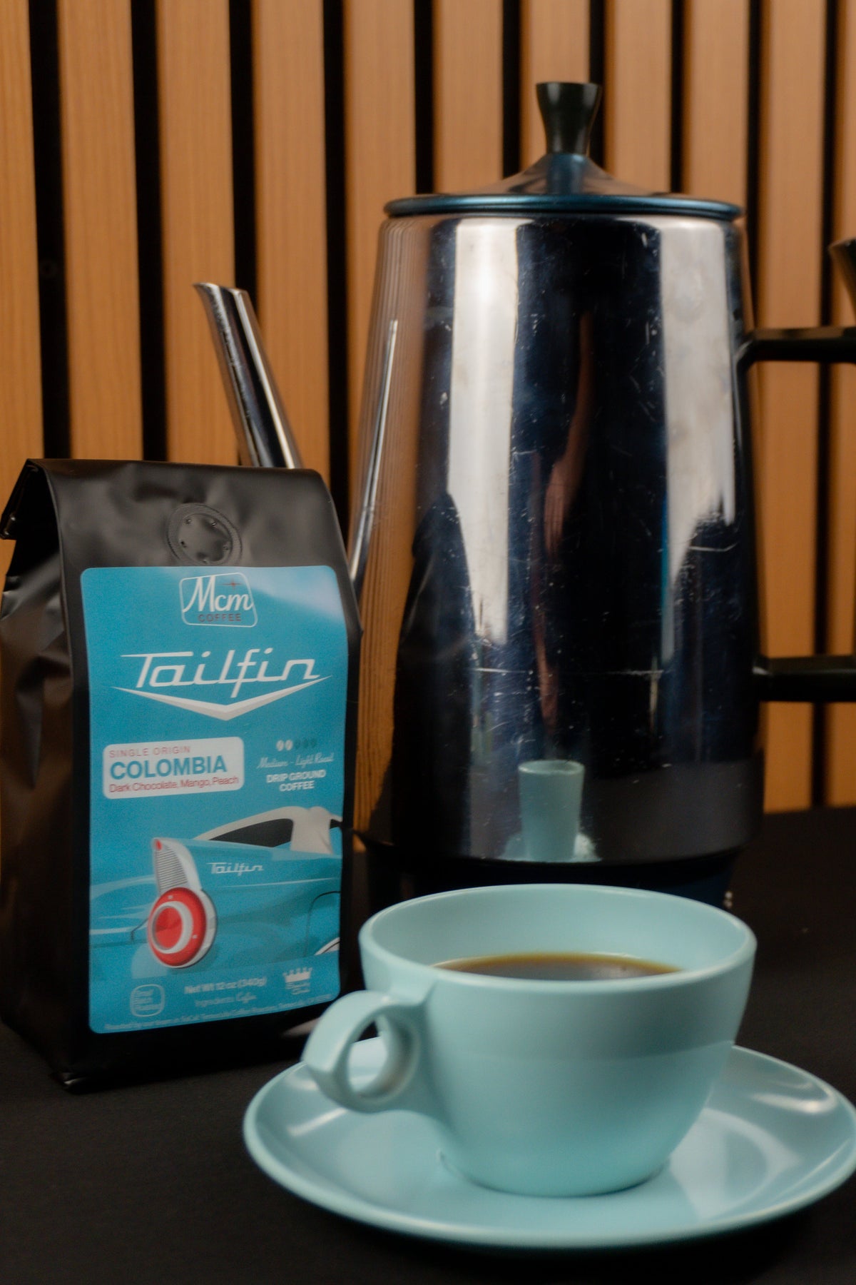 Turquoise cup of coffee with a Tailfin Colombia coffee bag and a French press in the background.